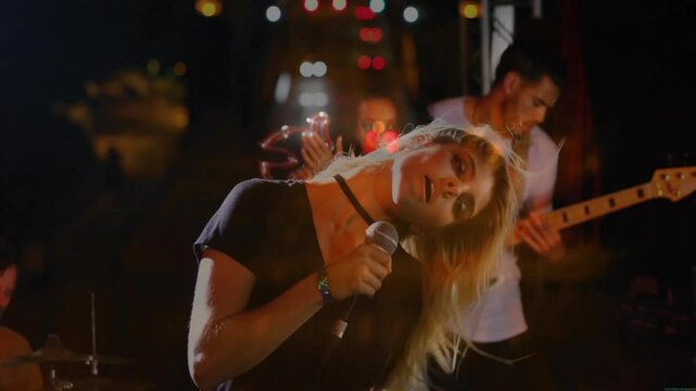 Singer gripping mic, singing on music stage, camera pulling back revealing band backing under bokeh