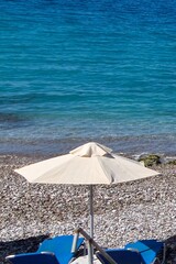 Serene vertical shot of a beach scene, highlighting the contrast between the light umbrella and the deep blue sea, perfect for travel concepts.