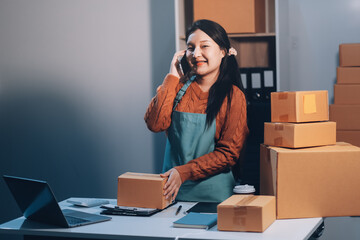 Startup SME small business entrepreneur of freelance Asian woman wearing apron using laptop and box to receive and review orders online to prepare to pack sell to customers, online sme business ideas.