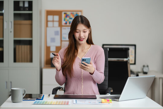 Female coder or developer working  using a smartphone and computer display in problem solving at workplace.