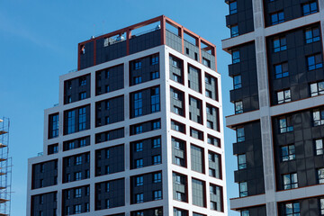 A modern building with a geometric design, white walls, red accents and large windows against a clear blue sky.