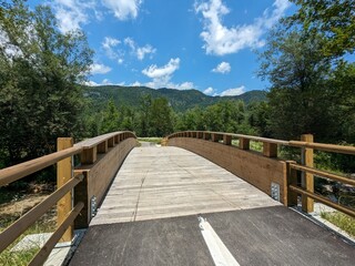 Wooden pedestrian bridge crossing a river in a scenic valley surrounded by Austrian Alps mountain peaks.