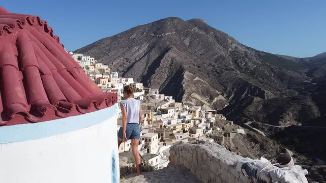 4k Cinematic Aerial Video of drone following woman to reveal Olympos Village, Karpathos: Close to Colorful Houses and Mountain