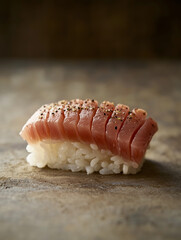 Delicious tuna nigiri resting on a textured surface with black pepper sprinkles