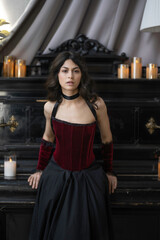 Portrait of sensual girl in red vintage velvet corset near piano with candles