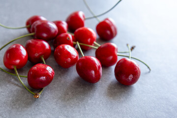 close-up of fresh red cherries scattered on gray background, side view