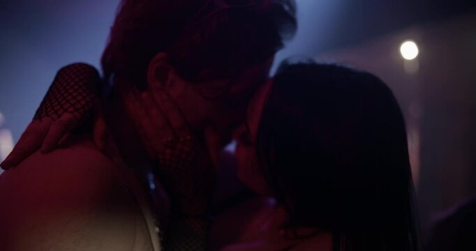 Caucasian Couple Sharing a Passionate Moment, Embracing and Kissing Under Colorful Lights and Pulsating Electronic Music. Diverse Male and Female Crowd Dancing in an Electrifying Nightclub