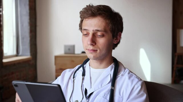 Professional man in lab coat holds tablet with both hands, scrolling through information attentively, fully engaged in medical review. Concept of modern medicine, digital records, smart care.