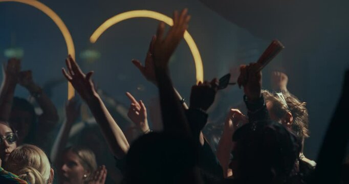 Diverse Party Crowd Enjoying Time in a Nightclub, Dancing Under Dynamic Lights and Pulsating Music. Young Men and Women Having an Emotional Night Out. Slow Motion Footage Focusing on Hands in the Air