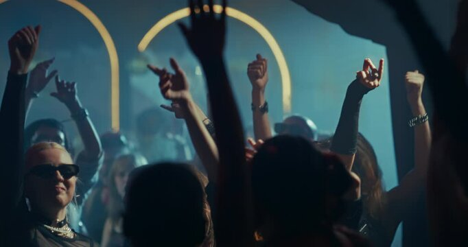 People Move to Energetic Techno Rhythms in a Dark Club with Flashing Stroboscopes. Cinematic Slow Motion Footage with Hands in the Air, Reaching for Lasers. Celebrating Nightlife and Youth Culture