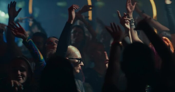 Diverse Party Crowd Enjoying Time in a Nightclub, Dancing Under Dynamic Lights and Pulsating Music. Young Men and Women Having an Emotional Night Out. Footage Focusing on Hands in the Air