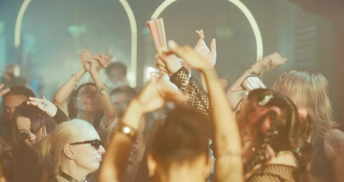 Slow Motion Footage of a Crowded Modern Nightclub with Diverse Beautiful People Raising Arms to Dynamic Electronic Music. Lights Pulse in Sync with the Beat. Ecstatic, Youthful and Hedonistic Mood