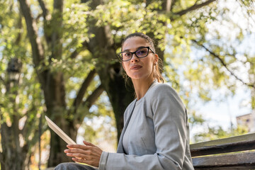 Young businesswoman sitting at park working on digital tablet, professional occupation worker, out...