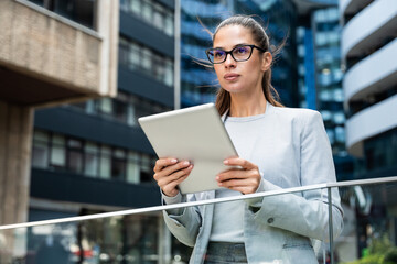 Professional woman standing confidently outside modern office building, interacting with digital...