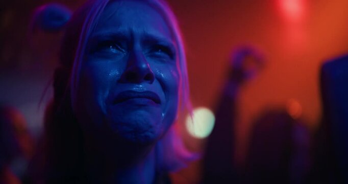 Close Up Portrait of a Sad Tired Young Woman with Teary Eyes Standing on a Dance Floor in a Crowded Nightclub. Surrounded by Flashing Lights and People, She Appears Distant and Overwhelmed