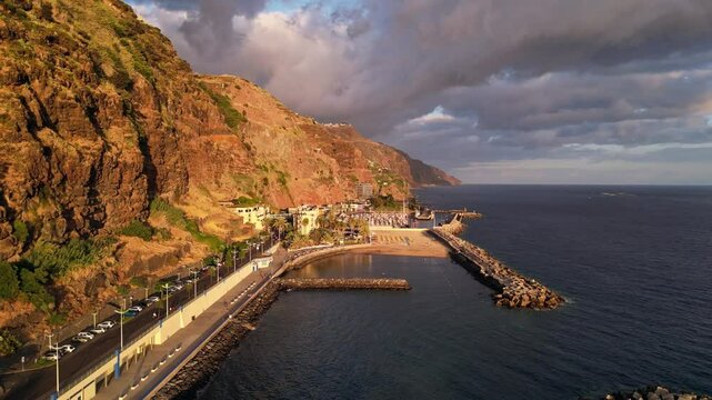 Dramatic cliffs and lush greenery of the coastline of Calheta Madeira, Portugal, at sunset.