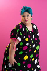 Colorful expressive big size woman posing in polka dot dress on pink background