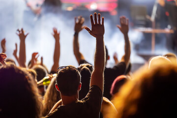 The audience gets excited and cheers with their arms raised during the concert of the musical band that performs on stage.