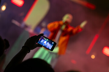 The audience records videos and takes photos with their smartphones during the concert of the musical band that performs on stage.