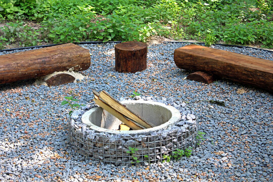 Fire pit with wooden outdoor bench in shape of a log on the camping site. Eco-friendly outdoor recreation. Log benches in the forest. Recreation area with benches made of wooden logs around fire pit.