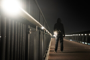 A crime concept of a mysterious hooded figure, standing on a path with glowing lights at night