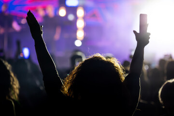 The audience gets excited and cheers with their arms raised during the concert of the musical band that performs on stage.