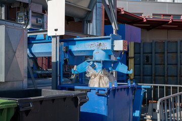 Industrial machine filling plastic bag in blue container outdoors at recycling plant