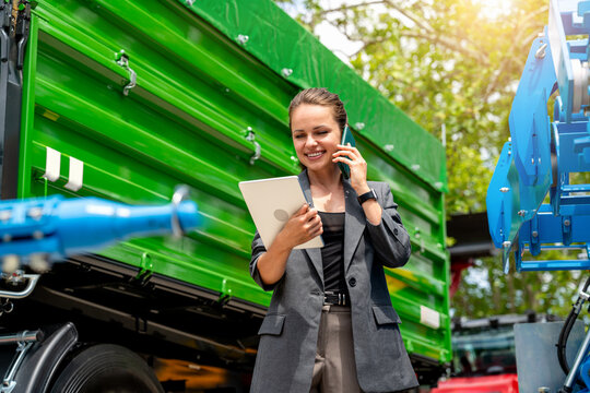 Businesswoman in suit communicating with client on phone while holding digital tablet at farm equipment dealer - Powered by Adobe