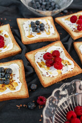 Flat lay of toasted white bread topped with labneh, fresh raspberries, blueberries, maple syrup, and flax seeds. Sweet breakfast or brunch idea with natural light and food styling