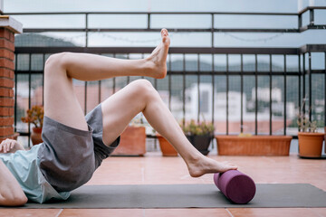 Woman performing single-leg hip bridge with foam roller for strength and stability