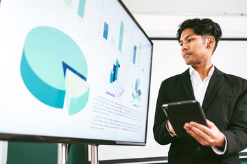 Business professional presenting financial data on a digital screen with tablet in hand, highlighting analytic, corporate strategy, and digital transformation in a modern office environment.
