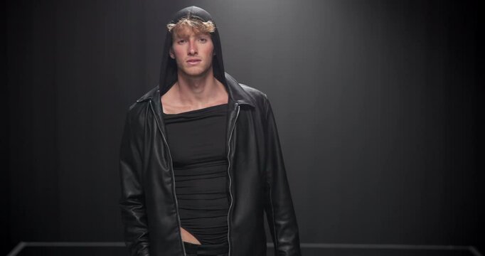 Fashion, walking and face of man on runway in designer brand, clothes and outfit at showcase event. Black background, catwalk and portrait of model on stage for couture, trendy collection and style