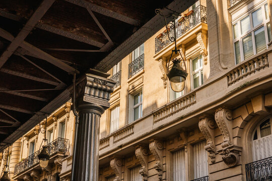 Ornate Parisian apartment building facade illuminated by golden sunlight, seen from under a bridge.