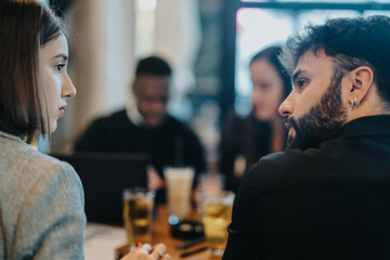 A diverse group of young professionals engaged in a thoughtful discussion and brainstorming session in a modern cafe, emphasizing collaboration and teamwork.