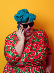 Joyful plus size woman talking on smartphone against orange background