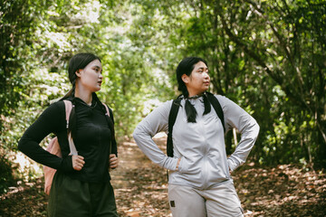 Two female friends with backpacks on vacation hiking through countryside together. Asian friend...