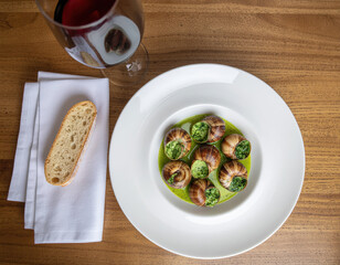 Classic escargots de Bourgogne, served in a rich green garlic-parsley butter sauce, alongside a glass of red wine and a slice of baguette.