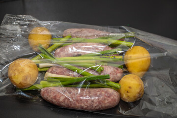 Meat sausages with potatoes in a baking sleeve in the oven. Raw grill sausages on a black background.