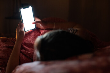 A young woman scrolls endlessly on her phone before sleep, face lit by the screen. Symbolic of modern tech habits and delayed sleep.