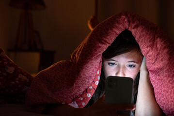 Sleep-deprived woman in bed illuminated by screen light, showing impact of screens on rest.