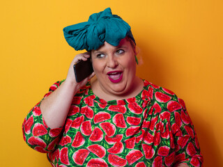 Joyful plus size woman talking on smartphone against orange background