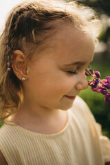 Fototapeta premium Close-up portrait of a little girl smelling a purple lupine flower. Soft natural light and peaceful expression. Childhood innocence, summer nature scene.