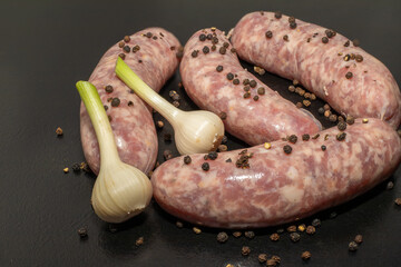 Meat sausages with garlic and sulphur peppercorns, prepared for grill, on black background. Raw...