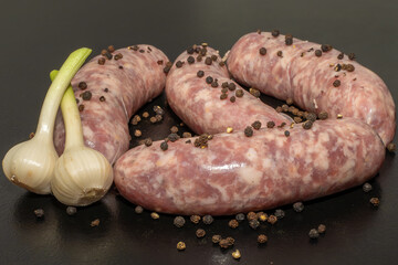 Meat sausages with garlic and sulphur peppercorns, prepared for grill, on black background. Raw...