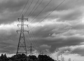 A striking black and white image of towering power lines and pylons stretching across a dramatic,...