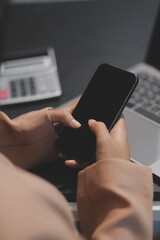 Young beautiful Asian businesswoman holding smartphone while working in the office room.