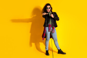 Young stylish man singing passionately into a microphone against a vibrant yellow background with a casual outfit