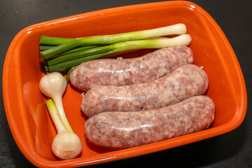 Meat sausages with garlic, prepared for grill, in an orange roasting pan. Raw sausages for grill.