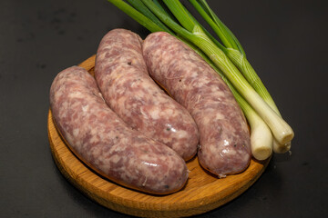 Meat sausages with garlic and green onions, prepared for grill, on a wooden board. Raw sausages for...