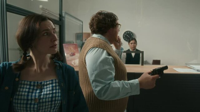 Medium full shot of agitated unprofessional male criminal discussing with female crime partner ransom terms while speaking to police on phone during bank robbery